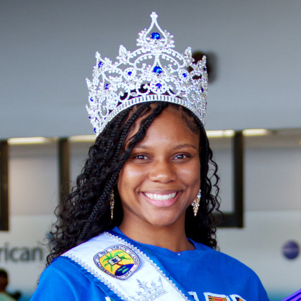 Image of Asha Hyndman, a smiling young woman with long braids wears an ornate silver and blue crown and a University of the Virgin Islands sash.